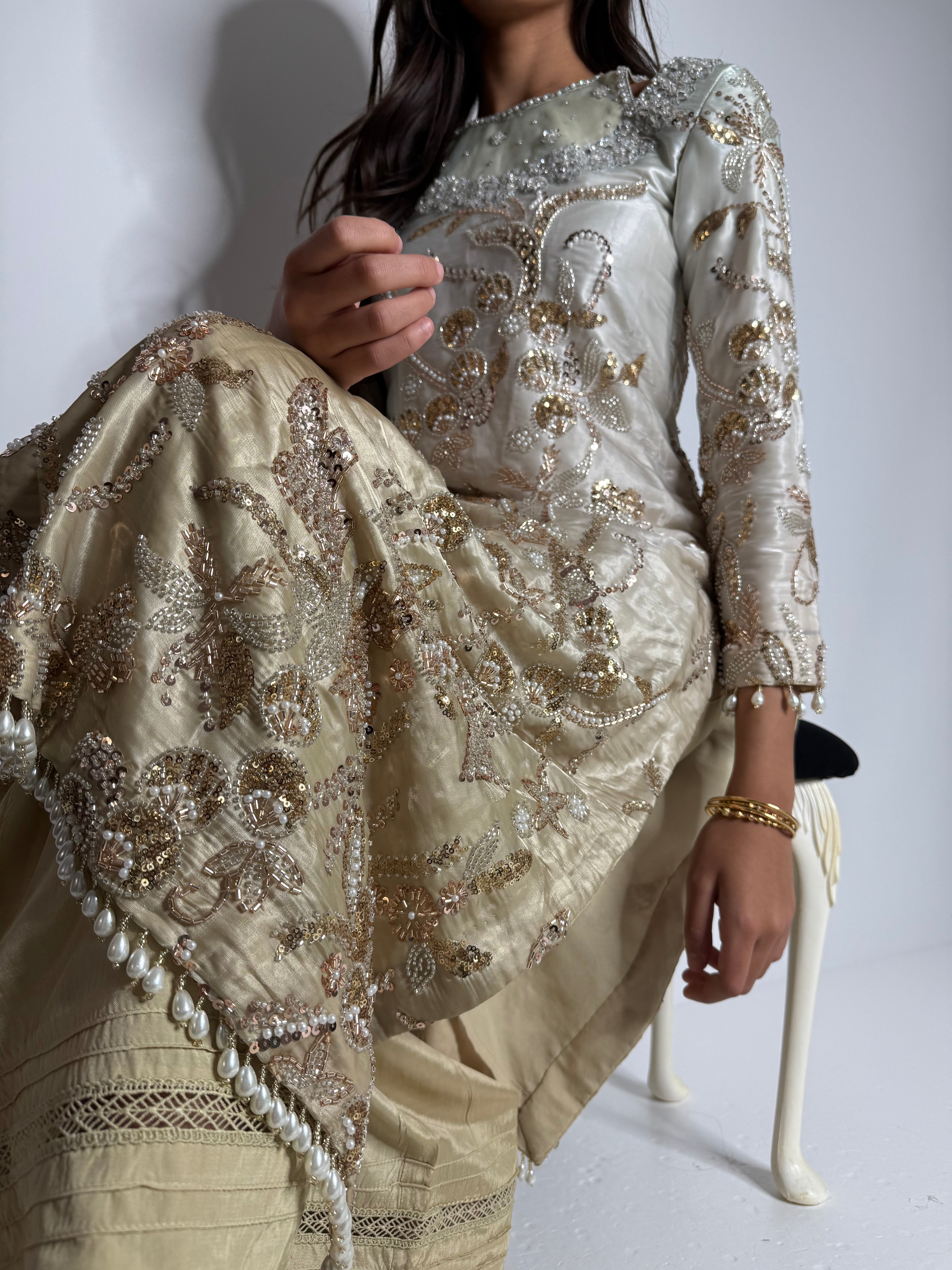 Model sitting, showcasing silk trousers and embellished dupatta details.