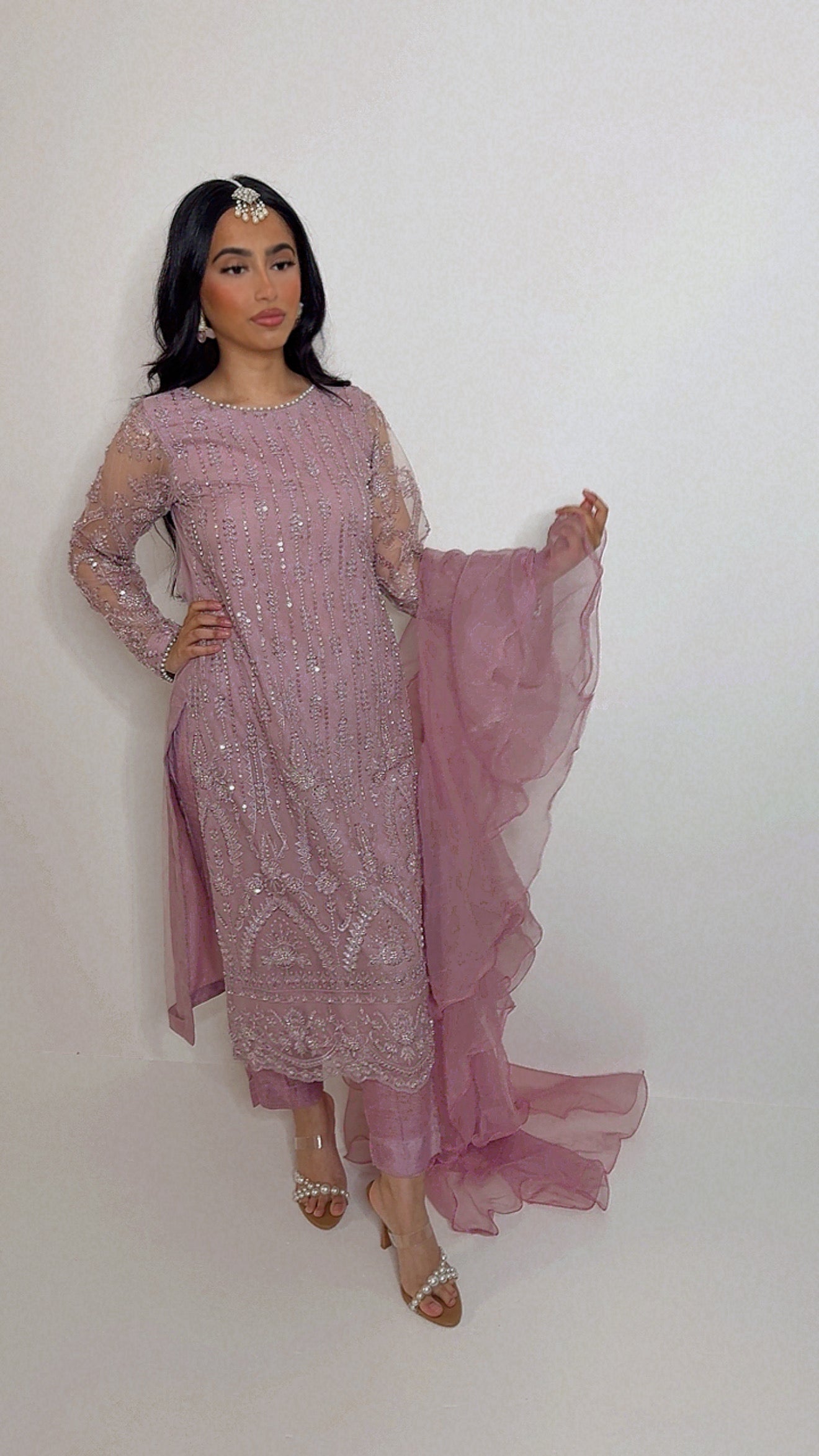 Woman wearing a pink embroidered traditional Pakistani outfit with a white background