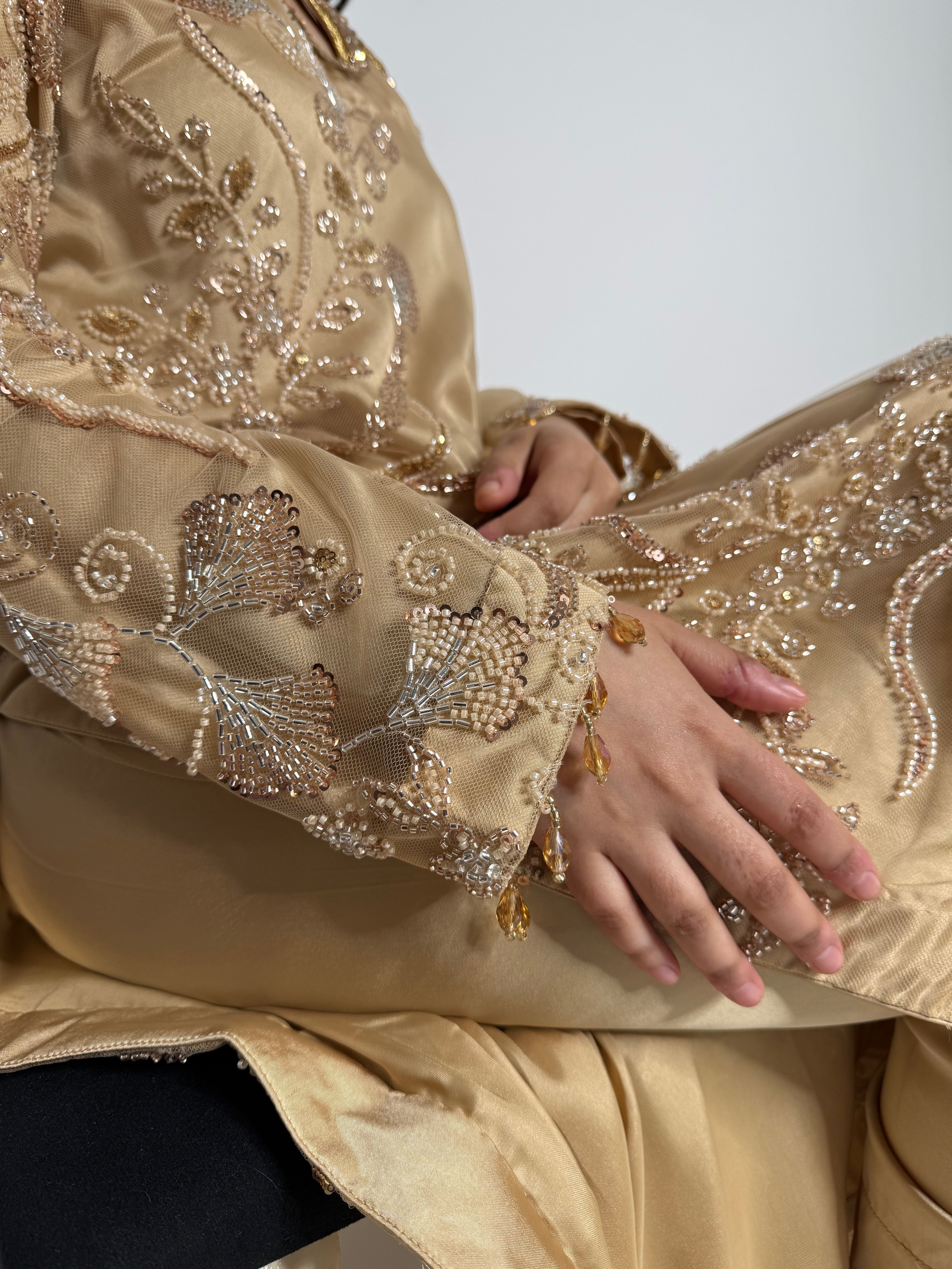 Close-up of a person wearing a gold embroidered Indian outfit with a plain background