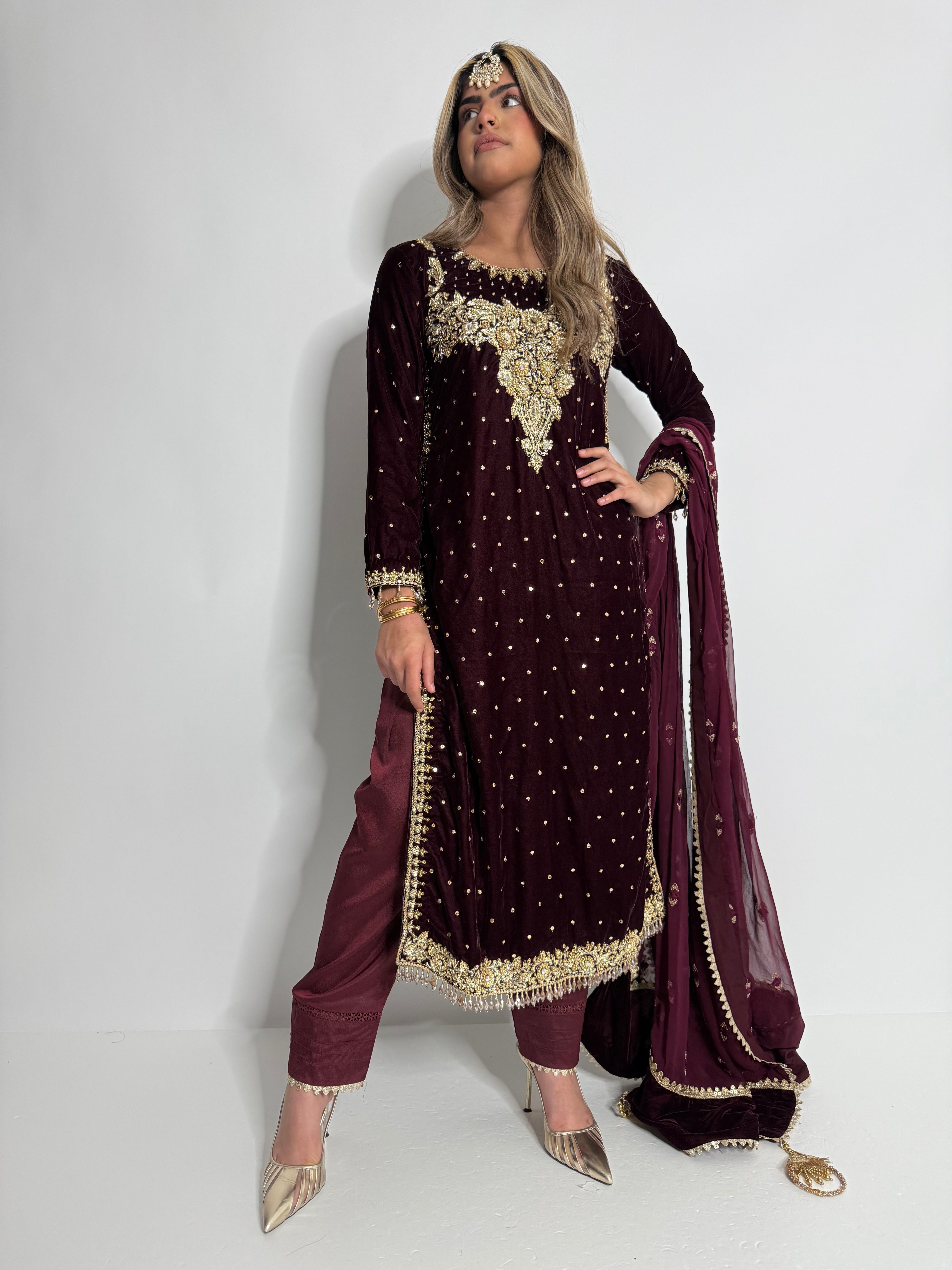 Model wearing Maeryn Maroon Velvet Pakistani Wedding Suit with golden handwork and chiffon dupatta.