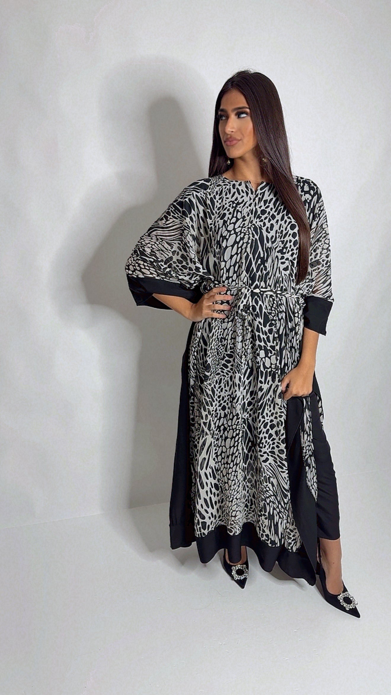 Model wearing a black and white printed kaftan outfit with belt, styled with trousers for a modest yet fashionable look.