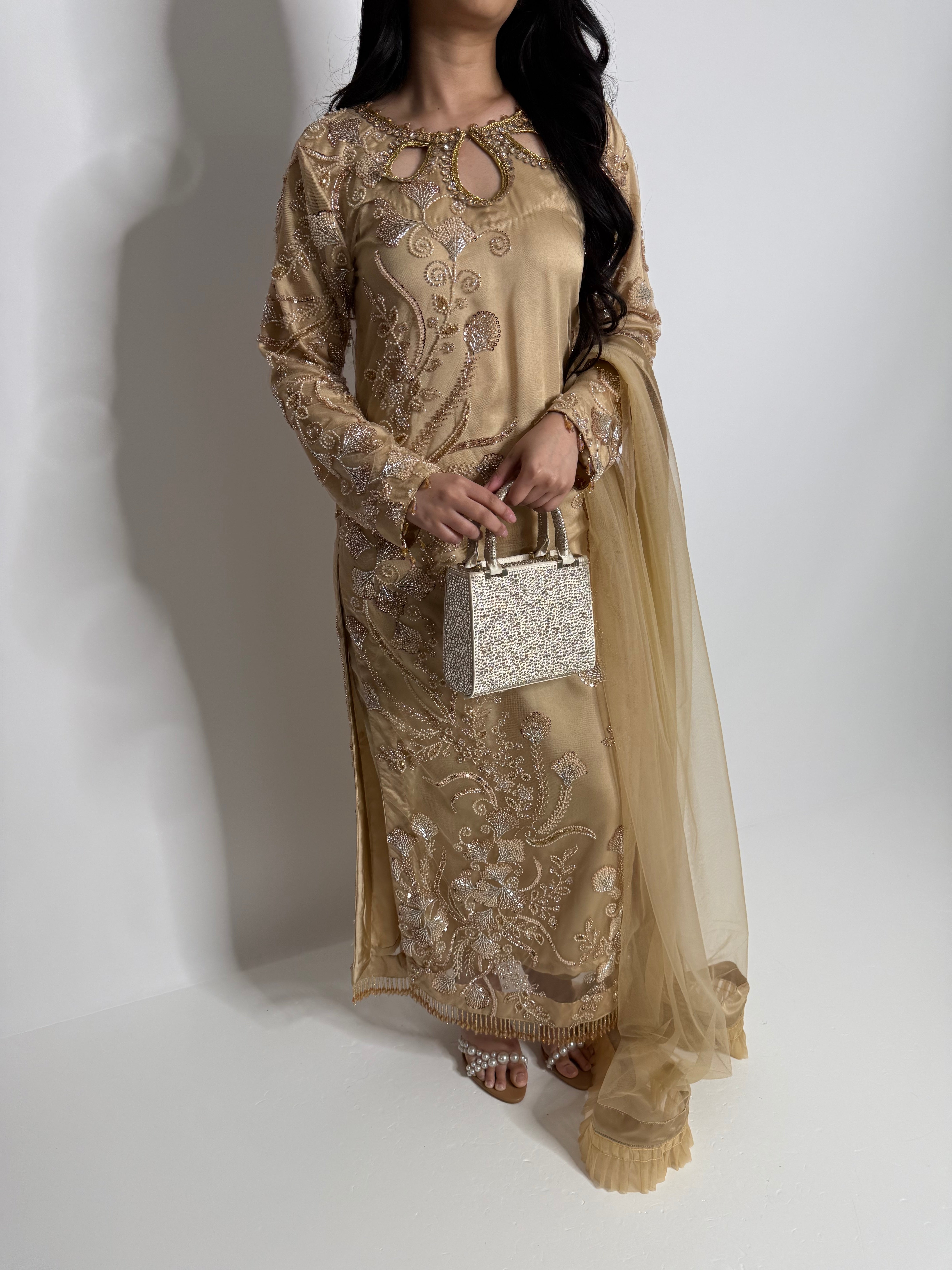 Person wearing a gold embroidered dress holding a clutch on a white background