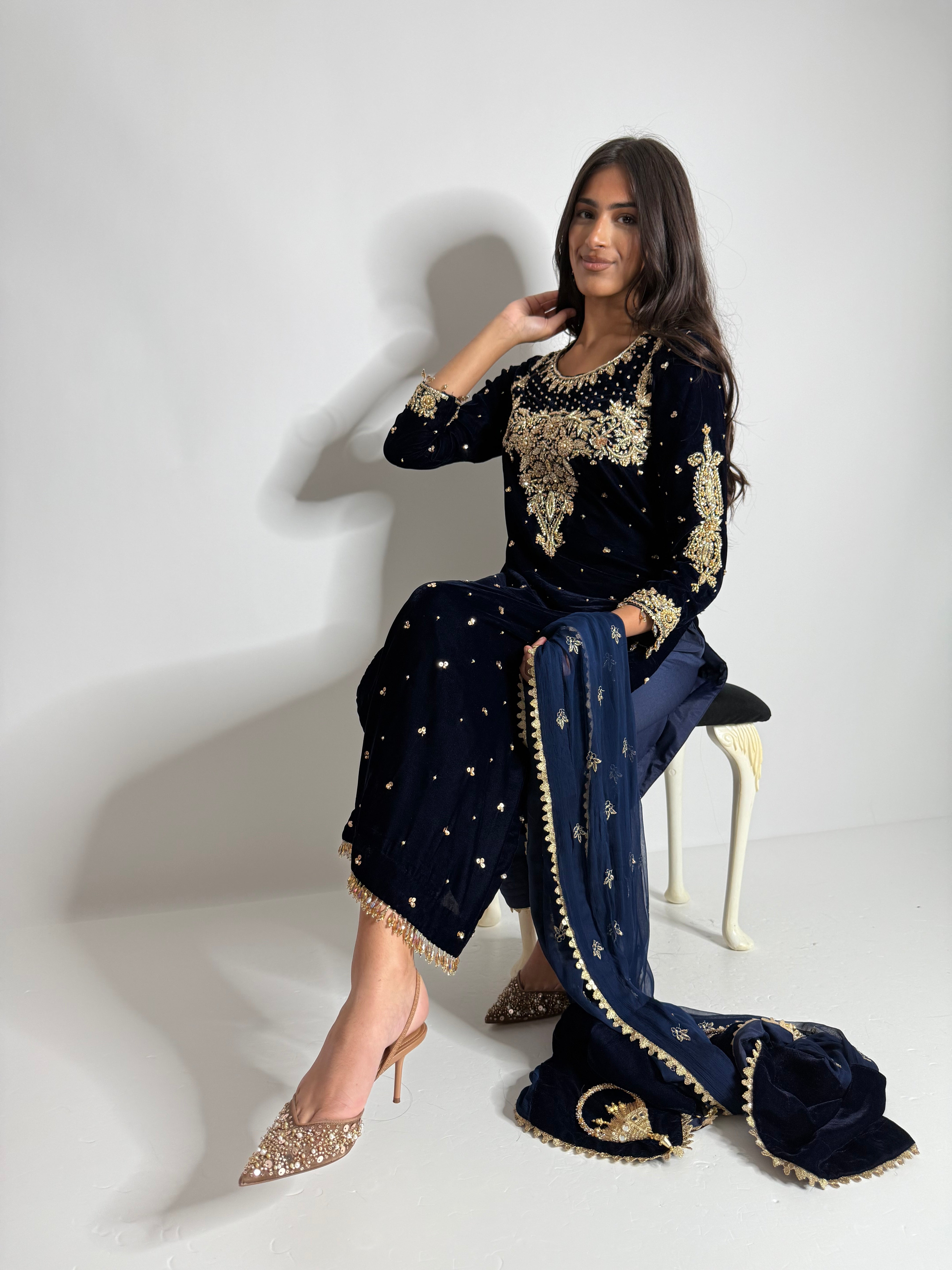 Model wearing Nerina Navy Velvet Pakistani Wedding Suit with golden handwork and chiffon dupatta.