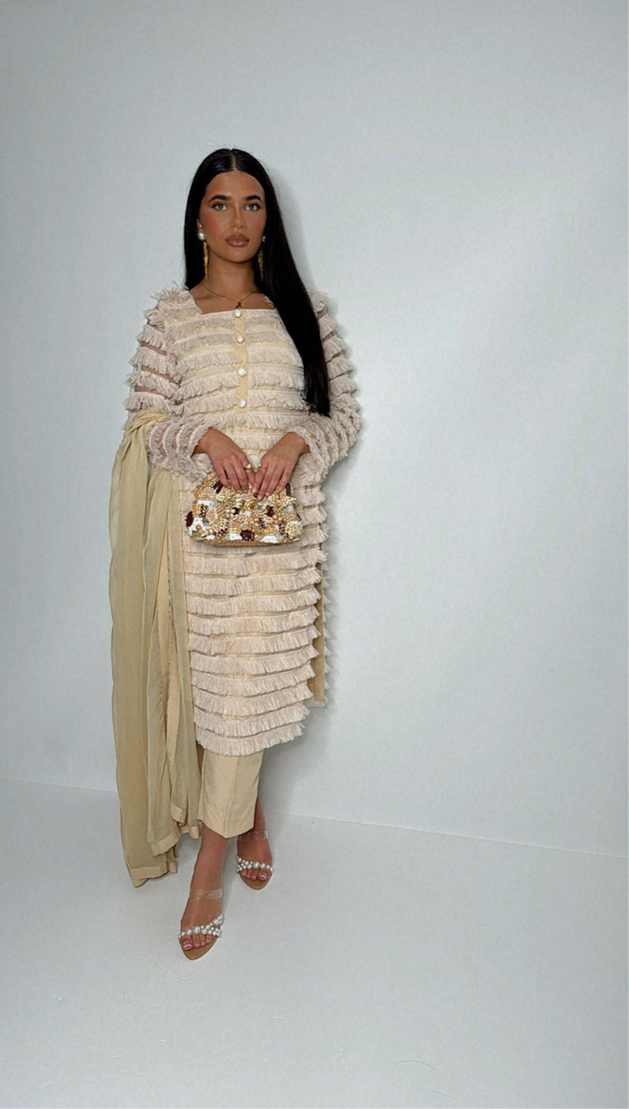 Model wearing a cream three-piece Pakistani suit with ruffle-panel kameez and chiffon dupatta — styled modestly for formal occasions.