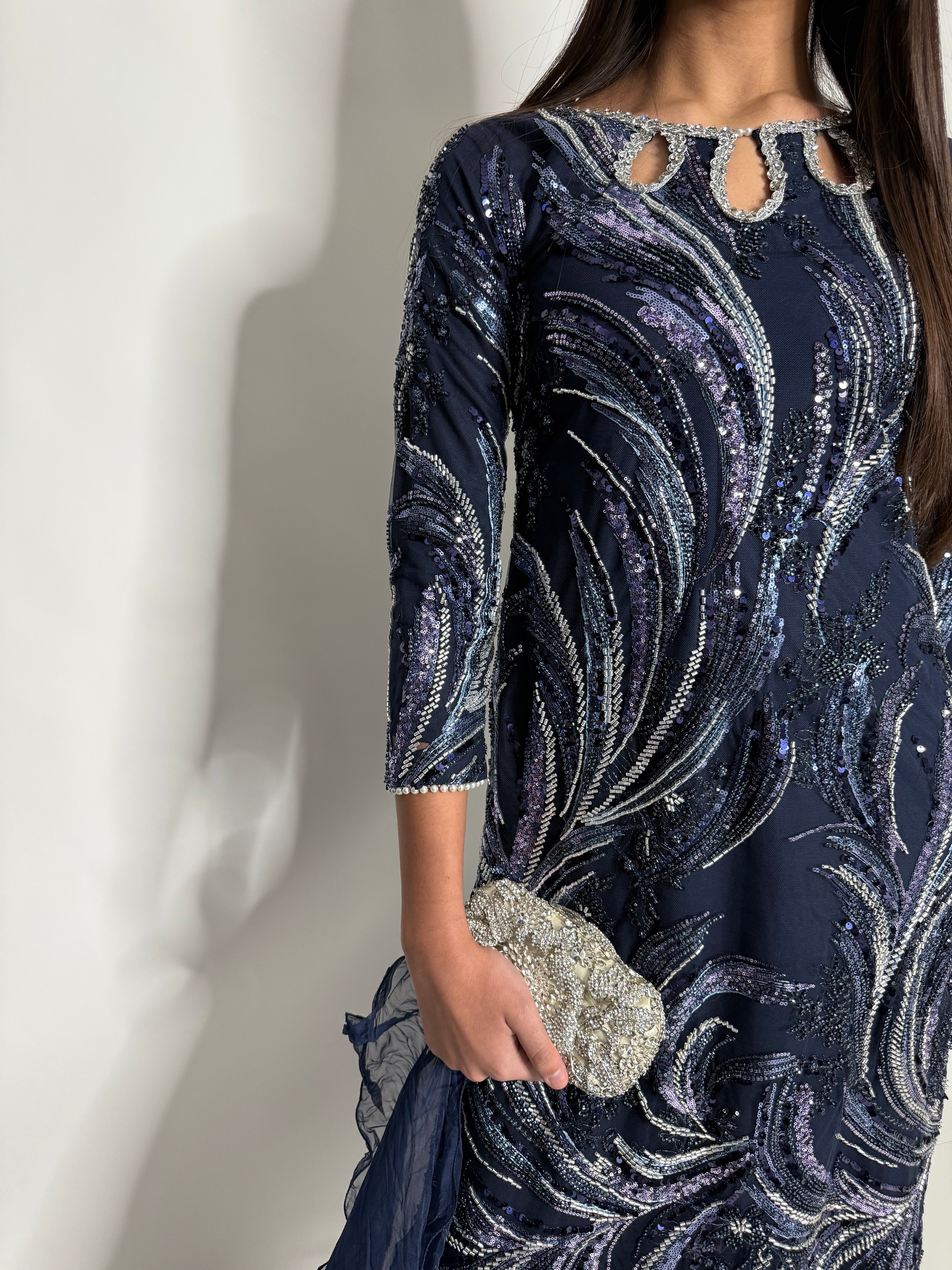 Close-up of a person wearing a dark blue dress with silver embellishments on a white background